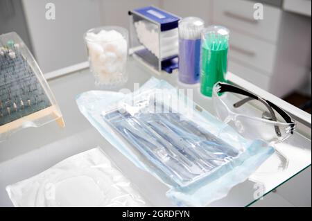 Nahaufnahme von zahnmedizinischen Instrumenten. Glastisch in der Zahnarztpraxis mit allen notwendigen Werkzeugen für die Zahnbehandlung: bohrköpfe, Gläser, Wangenaufroller, Stahlhaken Stockfoto
