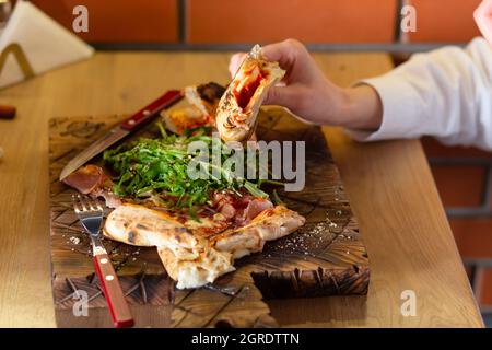 Nahaufnahme der Hände eines Mädchens, das in einem Café Bruschetta oder Pizza mit Kräutern und Sauce isst Stockfoto