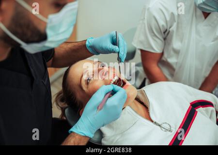 Kaukasische Patientin, die mit offenem, breitem Mund liegt, während die Krankenschwester operiert Stockfoto
