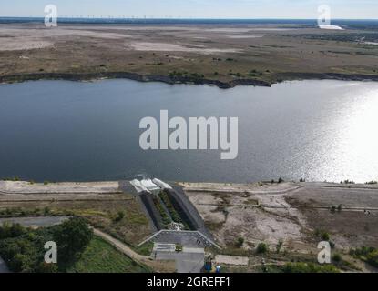 01. Oktober 2021, Brandenburg, Cottbus: Langsam füllt sich die ehemalige Braunkohlebergwerk Cottbus-Nord mit Wasser und wird so zur Cottbuser Ostsee (Luftaufnahme mit Drohne). Auch die Landmasse im oberen Teil des Fotos wird in den nächsten Jahren bis zu den Windturbinen im Hintergrund im Wasser verschwinden. Mitte April 2019 begann die Überschwemmung der ehemaligen Tagebaumine Cottbus-Nord. Das Energieunternehmen Lausitz Energie Bergbau AG (LEAG) lässt für das Hochwasser Wasser aus der Spree über den Hammergraben in das Tagebauloch fließen - rund 45 Millionen Kubikmeter pro Jahr Stockfoto