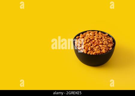 Weiße Bohnen in Tomatensauce in Schüssel isoliert auf gelbem Hintergrund Stockfoto