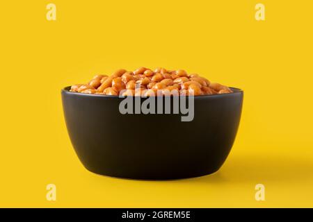 Weiße Bohnen in Tomatensauce in Schüssel isoliert auf gelbem Hintergrund Stockfoto