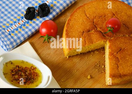 Maisbrot Kirschtomaten und Olivenöl auf Holzschneidebrett und blau-weiß kariert von direkt oben Stockfoto