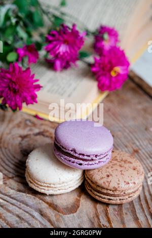 Macarons Hintergrund rote Blumen und Bücher, auf einem Holztisch. Vertikaler Rahmen. Ästhetik mit Makronen und Blumen. Schöne Kuchen auf einem Holztisch Stockfoto