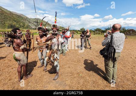 Indonesien, Papua, Stadt Wamena, westliche Touristen, die sich mit lokalen Stämmen fotografieren. Baliem Valley Cultural Festival, jedes Jahr im August kommen Stämme zusammen, um uralte Kriegsszenen aufzuführen, Parade und Tanz in traditioneller Kleidung Stockfoto