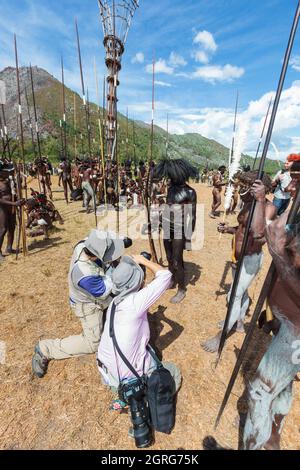 Indonesien, Papua, Stadt Wamena, asiatische Touristen fotografieren lokale Stämme. Baliem Valley Cultural Festival, jedes Jahr im August kommen Stämme zusammen, um uralte Kriegsszenen aufzuführen, Parade und Tanz in traditioneller Kleidung Stockfoto