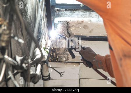 Ein asiatischer Arbeiter schweißen eine Stahlmarkise an die Decke eines Hauses. Stockfoto