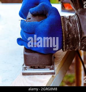 Arbeiten mit einer Schleifmaschine. Herrenhände in blauen Handschuhen arbeiten mit Elektrowerkzeugen Stockfoto