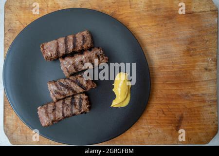 Traditionelles rumänisches Hackfleisch vom Grill, Mici oder Mititei auf einer schwarzen Keramikplatte mit Senf Stockfoto