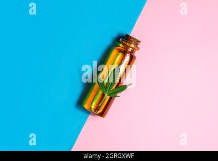 Medizinisches CBD Cannabisöl auf Glasflasche mit Marihuanablatt auf pastellrosa blauem Hintergrund Stockfoto