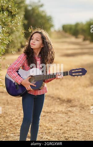 Brunette Mädchen spielt ihre Gitarre in einem Feld von Olivenbäumen bei Sonnenuntergang Stockfoto