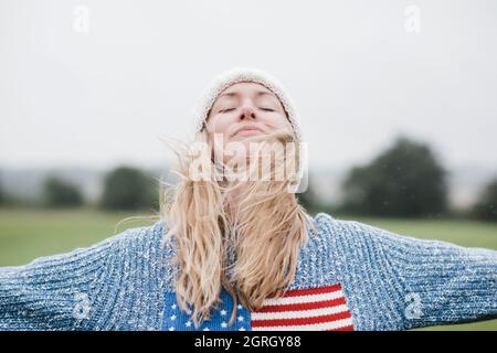 Die Frau trägt die amerikanische Flagge und genießt den Wind und den Regen in ihren Haaren Stockfoto