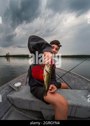 Happy teen junge hält einen Fisch, den er in einem Boot an einem stürmischen Tag gefangen. Stockfoto