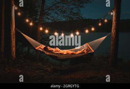 Pärchen, die an einem Sommerabend am See in einer Hängematte liegen. Stockfoto