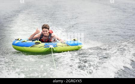 Ein glücklicher Teenager, der sich auf einer von einem Boot auf einem See gezogenen U-Bahn amüsieren kann. Stockfoto