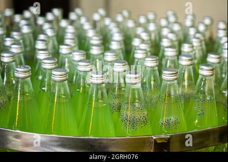 Gruppe von abgefülltem grünen Saft aus Glas auf einem Stahlförderer der Produktionslinie in der Getränkeverarbeitungsanlage Stockfoto