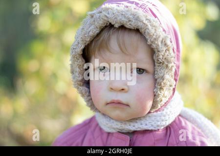 Ein kleines Kind in einer warmen Jacke mit einem traurigen Ausdruck. Stockfoto