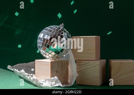 Stillleben mit Holzwürfeln und Diskokugel, die Sonneneruptionen vor smaragdgrünem Hintergrund reflektiert Stockfoto