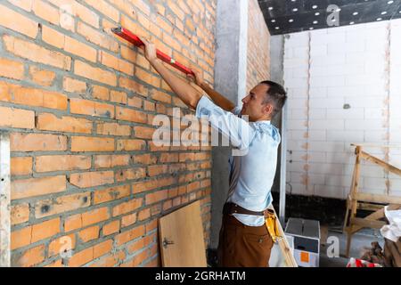 Junge Profi in leeren unfertigen Wohnung Messung der Wand mit Hilfe von Maßband, überprüfen Notizen. Reparatur- und Refurbishment-Konzept Stockfoto