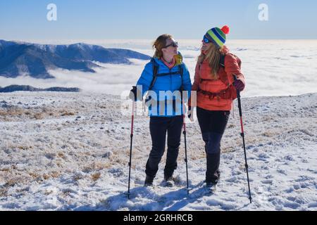 Zwei Wanderfrauen genießen sich in den Bergen von Leaota (Teil der Karpaten), Rumänien, mit einem Meer von Wolken hinter ihnen. Winter, Wandern, adve Stockfoto