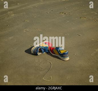 Bunte Turnschuhe liegen verlassen am Strand. Stockfoto