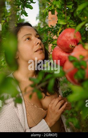 Porträt einer jungen Frau mit reifen roten Granatäpfeln Baum posiert. Konzept der gesunden Herbst und Winter Lebensstil und Ernährung, im Freien mit der Natur Stockfoto
