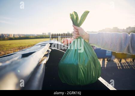 Mann, der mit Müll läuft. Plastikbeutel mit der Hand gegen Mülltonnen auf der Straße tragen. Stockfoto