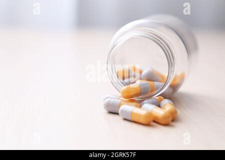 Pillen auf einem hellen Holztisch, Medikamente in Kapseln aus einer Plastikflasche verstreut. Konzept der Apotheke, Antibiotika, Vitamine Stockfoto