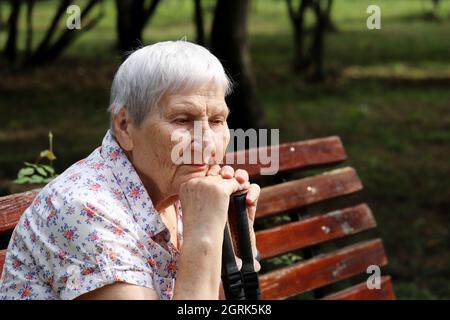 Ältere Frau mit friedlicher Gesichtsausdruck sitzt mit Gehstöcken auf einer Bank im Park. Leben im Alter, Rentenkonzept Stockfoto