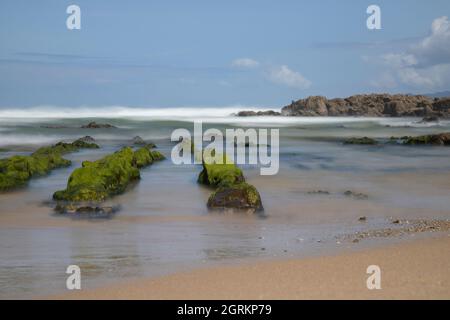 As Furnas Strand Langzeitbelichtung Bild zeigt ausgedehnte Felsen von grünen Algen unter einem blauen Himmel in Galicien bedeckt Stockfoto