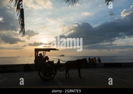 Fahrer einer zweirädrigen Pferdekutsche (Kalesa) und einige Jugendliche genießen den Sonnenuntergang auf dem Baywalk in Manila, Philippinen. Stockfoto