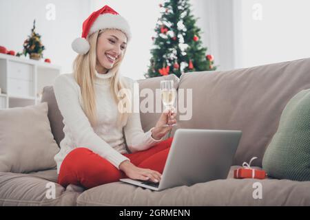 In voller Länge Körpergröße Foto blonde Frau trinken Champagner auf dem Sofa sitzen bekam Videoanruf auf Laptop Stockfoto