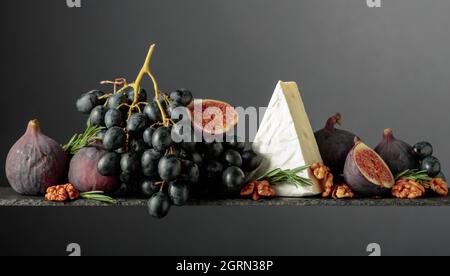 Käsebrie mit Feigen, Walnüssen und blauen Trauben auf dunklem Grund. Speicherplatz kopieren. Stockfoto