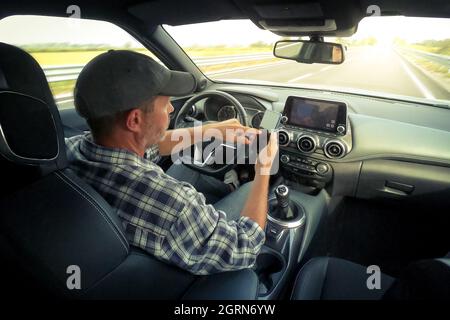 Mann fährt ein Auto und nutzt Infotainment. Der Fahrer liest Nachrichten und telefoniert während der Fahrt. Gefährliches Verhalten, Unfallrisiko. Gefahr, trans Stockfoto