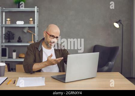 Geschäftsmann, der im Heimbüro am Schreibtisch sitzt und Online-Geschäftstreffen auf einem Laptop führt Stockfoto