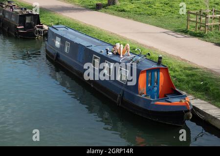 Blaues Schmalboot, das auf dem River Cam festgemacht ist, mit einem Mann, der auf dem Dach liegt, und entspannendem Lesen mit dem Fahrrad, auch auf dem Dach von Cambridge England Stockfoto