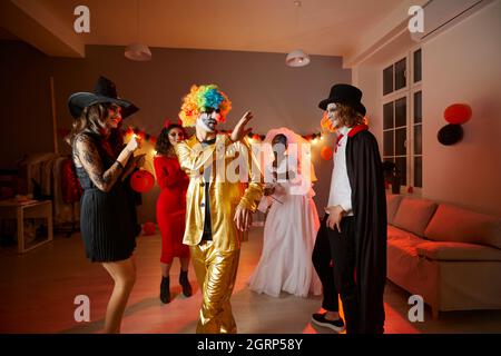 Fröhliche junge Freunde, die in Kostümen verkleidet sind und auf einer lustigen Halloween-Party zu Hause tanzen Stockfoto
