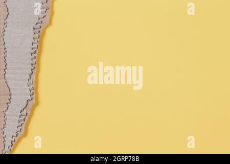 Altes braunes Wellpappenstück mit zerlumpter Kante auf pastellgelbem Hintergrund Stockfoto