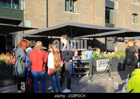 Freunde treffen sich von Caravan Kings Cross in herbstlicher Sonne auf dem Granary Square, bei Kings Cross, im Norden Londons, Großbritannien Stockfoto