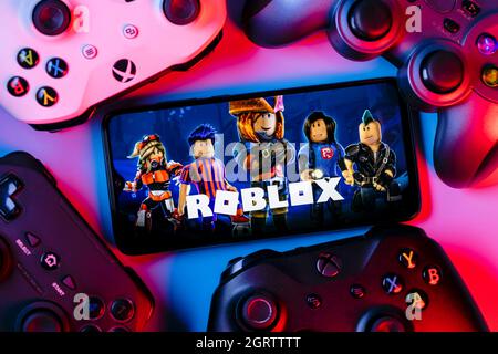 Roblox ist eine Online-Spielplattform und ein System zur Erstellung von Spielen. Ein Smartphone mit dem Roblox-Logo auf dem Bildschirm, umgeben von Gamepads. Stockfoto