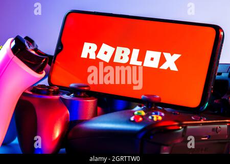 Roblox ist eine Online-Spielplattform und ein System zur Erstellung von Spielen. Ein Smartphone mit dem Roblox-Logo auf dem Bildschirm auf dem Stapel der Gamepads. Stockfoto