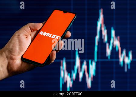 Roblox ist eine Online-Spielplattform und ein System zur Erstellung von Spielen. Ein Smartphone mit dem Roblox-Logo in der Hand. Aktiendiagramm im Hintergrund. Stockfoto