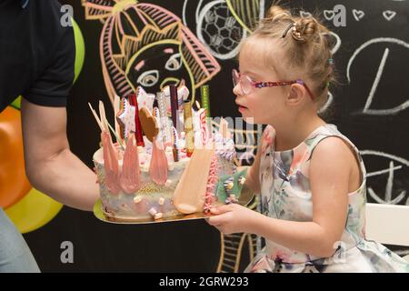 Ein Mädchen mit Down-Syndrom bläst an ihrem Geburtstag Kerzen auf einen Kuchen und wünscht sich Stockfoto