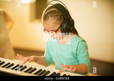 Ein Mädchen mit Down-Syndrom lernt Klavier spielen und hört Musik Stockfoto