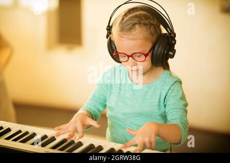 Ein Mädchen mit Down-Syndrom lernt Klavier spielen und hört Musik Stockfoto