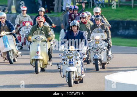 Quadrophenia-Schauspieler Phil Daniels beim Goodwood Revival 2014 führte eine Gruppe von „Mods“ auf der Rennstrecke an und fuhr mit einem Motorroller in Retro-Kleidung Stockfoto