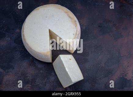 Alter Cheddar-Käse. Käse mit Reifung. Gealtertes Cheddar-Käserad auf dunklem Holzboden. Stockfoto