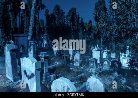 Friedhof im Wald an Halloween, beängstigender Friedhof mit Nebel und Fledermäusen in gruseliger Nacht. Steingräber in dunklen Nebelwäldern. Gespenstischer Ort mit Gräbern Stockfoto