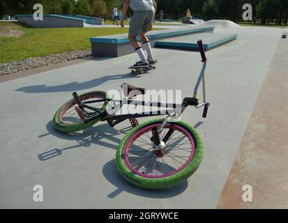 Dobrograd, Region Wladimir, Russland. 29. Juli 2017. BMX Bike liegt auf der Strecke im Skatepark. Teen auf Skateboard führt einen Trick auf dem Hintergrund Stockfoto