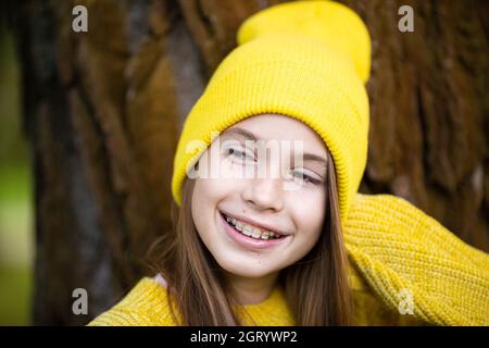 Portrait von modernen glücklichen Teenager-Mädchen mit Zahnspangen in gelben Kleidern im Park gekleidet. Hübsches Teenager-Mädchen mit Zahnspangen lächelt fröhlich. kinderg.a. Stockfoto